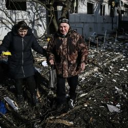 Unas personas pasan junto al cuerpo de un familiar frente a un edificio destruido tras los bombardeos sobre la ciudad de Chuguiv, en el este de Ucrania, mientras las fuerzas armadas rusas intentan invadir Ucrania desde varias direcciones. | Foto:ARIS MESSINIS / AFP