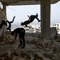 Jóvenes sirios aficionados al "parcours", practican movimientos acrobáticos y saltos hacia atrás, en la ciudad siria de Ariha, devastada por la guerra, en la provincia noroccidental de Idlib, controlada por los rebeldes. | Foto:AAREF WATAD / AFP