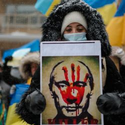 Una mujer sostiene un retrato del presidente ruso Vladimir Putin con una mano ensangrentada en la cara mientras miembros de la comunidad ucraniana protestan frente al Consulado General de la Federación Rusa en Montreal, Quebec. | Foto:Andrej Ivanov / AFP