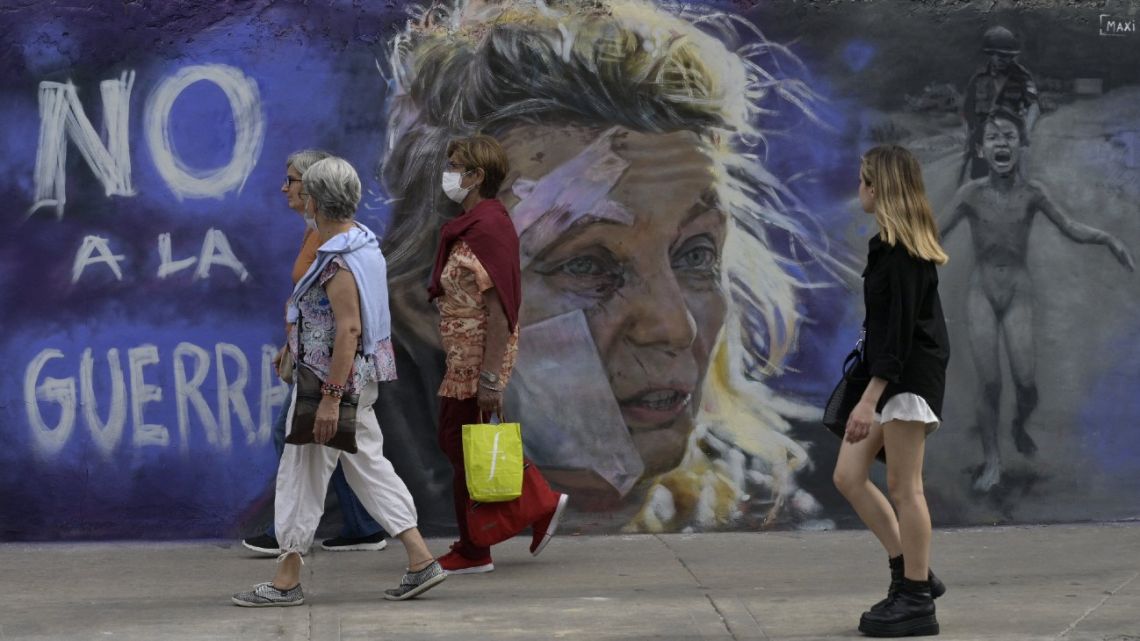 Women walk pass the mural reading 'No to war' by artist Maximiliano Bagnasco in Buenos Aires on March 5, 2022. Bagnasco painted this mural against the war inspired by two iconic images the portrait of Helena (centre), a 53-year-old teacher standing outside a hospital after the bombing of the eastern Ukraine town of Chuguiv on February 24, 2022, as Russian Armed Forces invaded Ukraine, taken by AFP Greek photojournalist Aris Messinis, and Kim Phuc Phan Thi, also known as 'Napalm Girl,' the iconic 1972 Vietnam War photograph taken by photographer Nick Ut of AP.