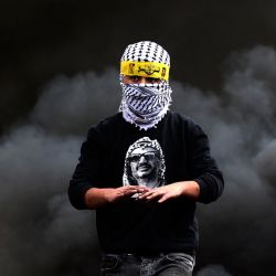 Un joven palestino con una camiseta con la imagen del difunto líder Yasser Arafat, pasa junto a unos neumáticos ardiendo durante los enfrentamientos con las fuerzas de seguridad israelíes, tras una manifestación contra la expropiación de tierras por parte de Israel, en la aldea de Kfar Qaddum, cerca del asentamiento judío de Kedumim. | Foto:JAAFAR ASHTIYEH / AFP