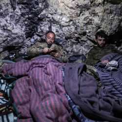 Un combatiente de la coalición rebelde siria "Frente Nacional para la Liberación" utiliza un teléfono mientras está tumbado en una cama improvisada, en una cueva en la zona montañosa del norte de la provincia noroccidental de Latakia. | Foto:OMAR HAJ KADOUR / AFP