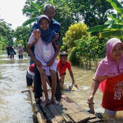 Una mujer jala una embarcación de madera llevando a su familia en el agua de la inundación después de asistir a una ceremonia de boda, en Cilacap, Java Central, Indonesia. | Foto:Xinhua/Anang Firmansyah