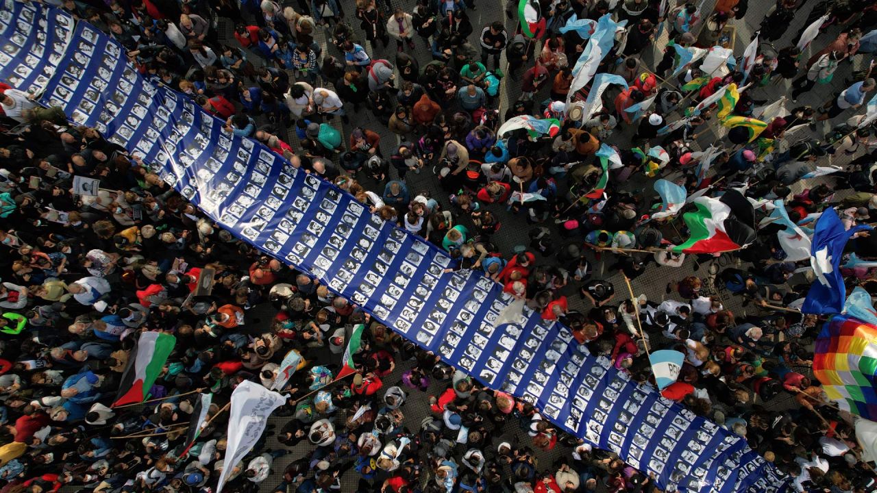 En esta vista aérea cientos de personas portan una gran pancarta con retratos de personas desaparecidas durante la dictadura militar (1976-1983) en el marco de una concentración para conmemorar el 46º aniversario del golpe, en la Plaza de Mayo de Buenos Aires. - Unas 30.000 personas desaparecieron tras ser detenidas durante el régimen militar de derecha acusadas de ser simpatizantes de la izquierda o consideradas subversivas, según organismos de Derechos Humanos. | Foto:ELENA BOFFETTA / AFP