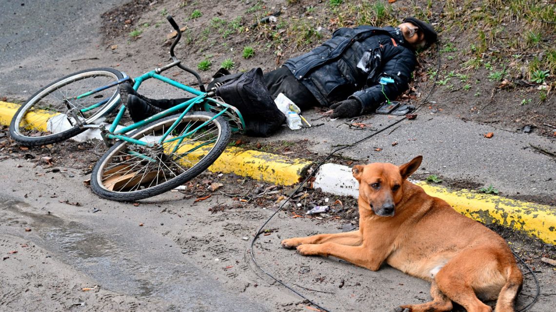 A dog lies next to the body of a man, in the town of Bucha, not far from the Ukrainian capital Kyiv on April 3, 2022. US and NATO leaders voiced shock and horror April 3, 2022, at new evidence of atrocities against civilians in Ukraine, and warned that Russian troop movements away from Kyiv did not signal a withdrawal or end to the violence. The Kremlin on rejected accusations that Russian forces were responsible for killing civilians near Kyiv.