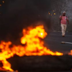 Hombres caminan cerca de neumáticos incendiados en la carretera Panamericana durante un bloqueo de carreteras en el marco de una huelga parcial de transportistas de carga y pasajeros, en Ica, en el sur de Perú. | Foto:ERNESTO BENAVIDES / AFP
