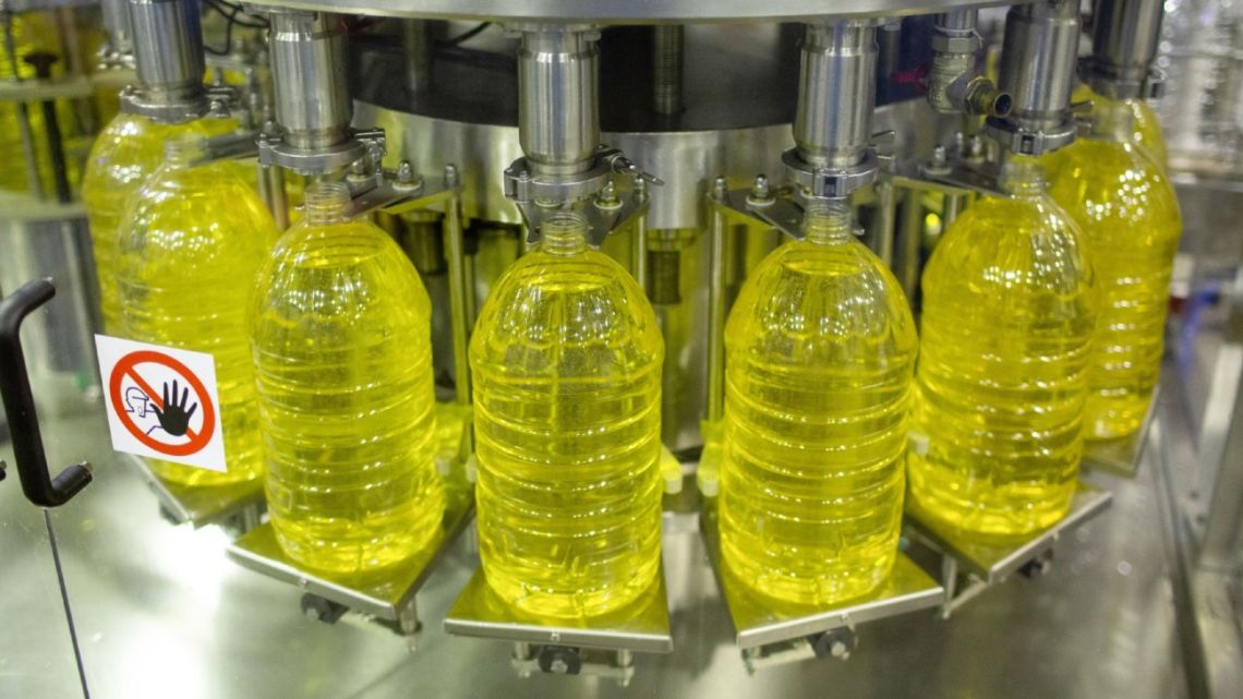 A machine dispenses sunflower oil into large plastic bottles on a production line.
