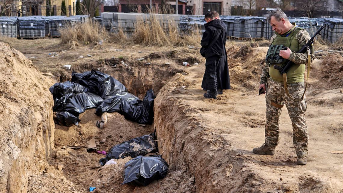 A Ukranian soldier looks at body bags as priests pray at a mass grave in the grounds surrounding the St Andrew church in Bucha, on April 7, 2022, amid Russia's military invasion launched on Ukraine. 