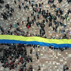 Una fotografía aérea muestra a los manifestantes sosteniendo una enorme bandera ucraniana en la plaza principal de Tirana, mientras se preparan para marchar hacia la embajada rusa. - Los manifestantes se reúnen frente a la embajada rusa en Tirana para protestar contra la invasión rusa en Ucrania. | Foto:GENT SHKULLAKU / AFP