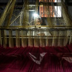 En esta fotografía un trabajador utiliza un telar manual para tejer un sari de seda Banarasi en un taller de Benarés. - Los tejedores manuales de Varanasi han cultivado una reputación de excelencia a lo largo de los siglos, especializándose en patrones intrincados, diseños florales y brocados dorados. | Foto:MONEY SHARMA / AFP