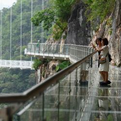 Visitantes en la sección de la pasarela del puente de cristal de Bach Long en el distrito de Moc Chau, en la provincia vietnamita de Son La, el 29 de abril de 2022. - Vietnam inauguró una nueva atracción para los turistas con la apertura de un puente con fondo de cristal suspendido a unos 150 metros por encima de un exuberante desfiladero cubierto de selva. | Foto:NHAC NGUYEN / AFP