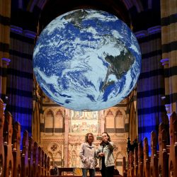 Un grupo de personas observa un globo terráqueo gigante de siete metros de diámetro -una obra de arte titulada "Gaia" del artista Luke Jerram- que está suspendido y gira desde el techo de la Catedral de San Pablo en Melbourne. | Foto:William West / AFP