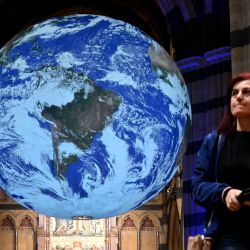 Una personas observa un globo terráqueo gigante de siete metros de diámetro -una obra de arte titulada "Gaia" del artista Luke Jerram- que está suspendido y gira desde el techo de la Catedral de San Pablo en Melbourne. | Foto:William West / AFP