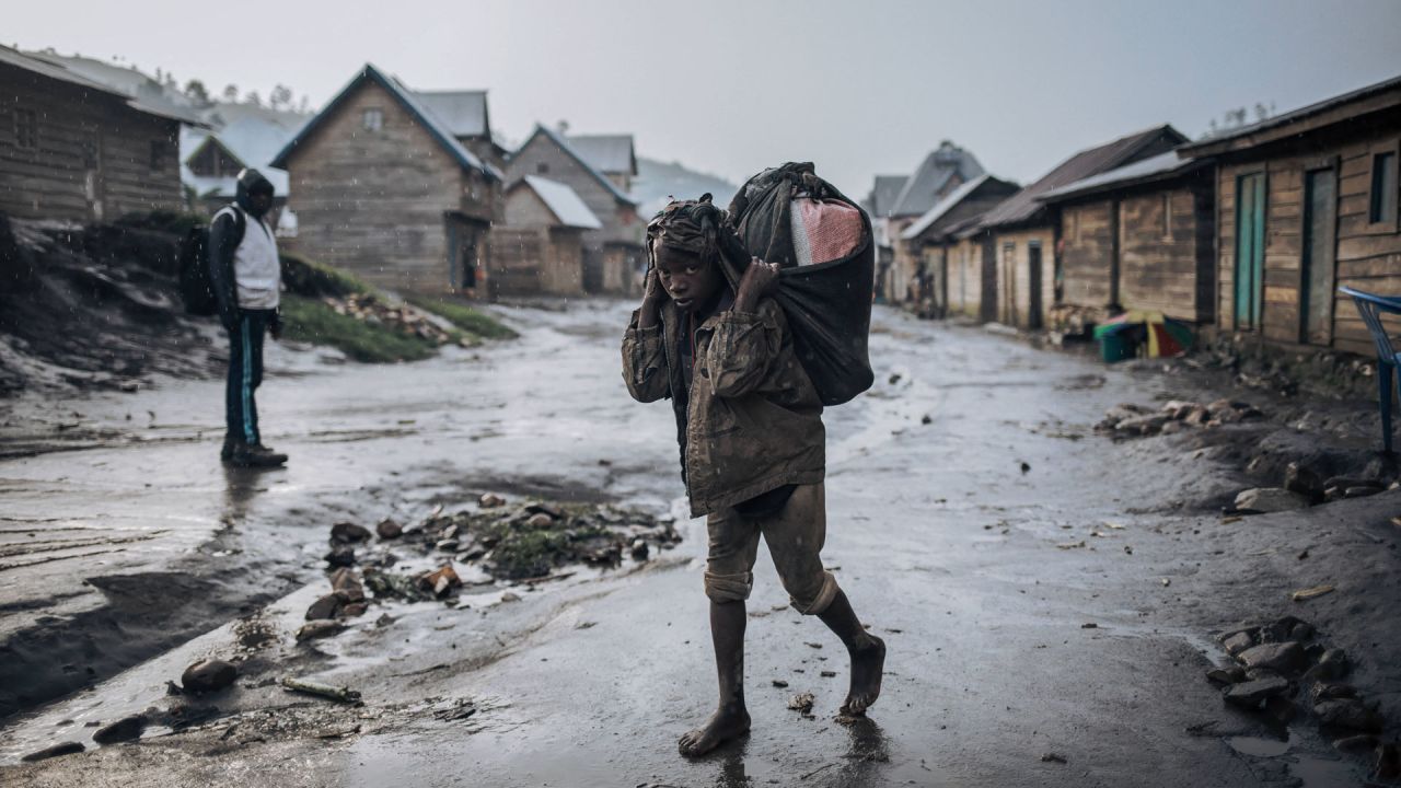 Un niño lleva mercancías a la espalda bajo la lluvia en la calle principal de Muheto, a tres horas de viaje en motocicleta desde el centro de Masisi, en las montañas donde los grupos armados atacan regularmente, en la provincia de Kivu del Norte, al este de la República Democrática del Congo. | Foto:ALEXIS HUGUET / AFP