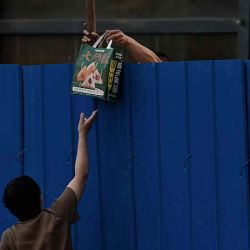 Una mujer le pasa comida a un hombre confinado en una zona residencial cercada bajo encierro debido a las restricciones del coronavirus Covid-19 en Beijing. Noel Celis / AFP | Foto:AFP