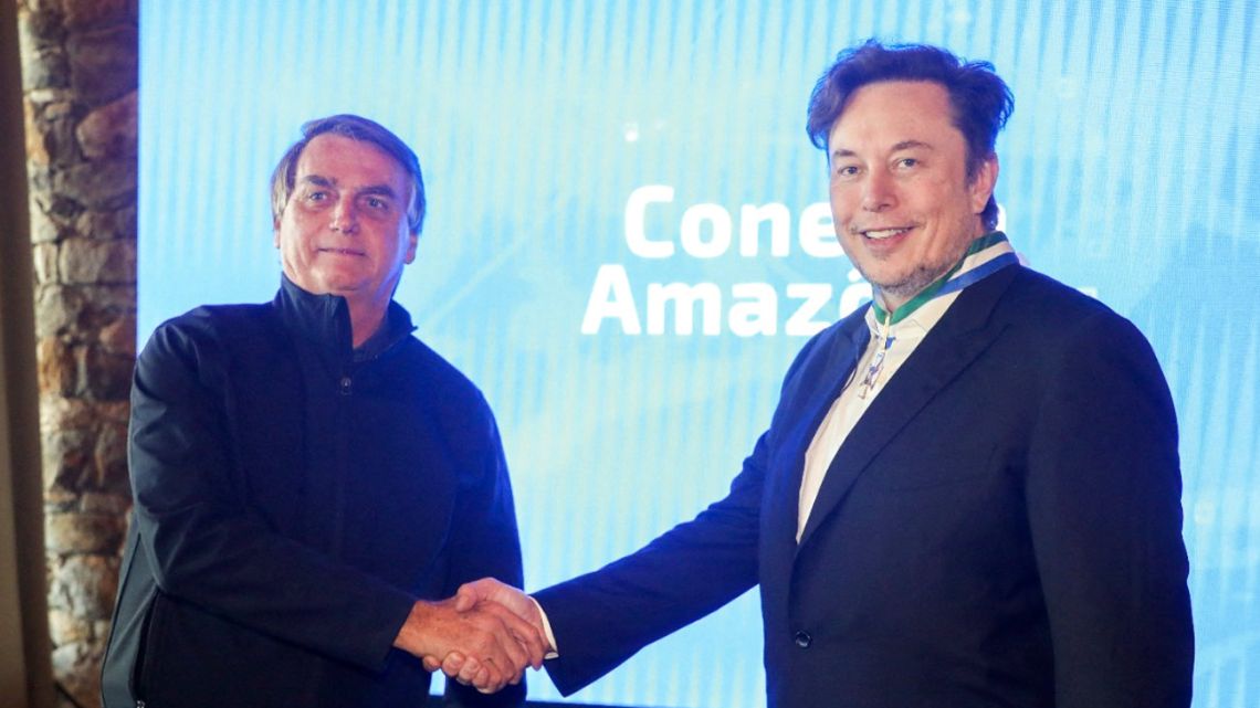 In this handout picture released by Brazil's Ministry of Communication, President Jair Bolsonaro  shakes hands with Elon Musk, at the event Conecta Amazonia in Porto Feliz, Sao Paulo state, Brazil on May 20, 2022. Billionaire Elon Musk, on a visit to Brazil Friday, announced a project to bring internet access to schools in the Amazon and improve satellite monitoring of the rainforest. 