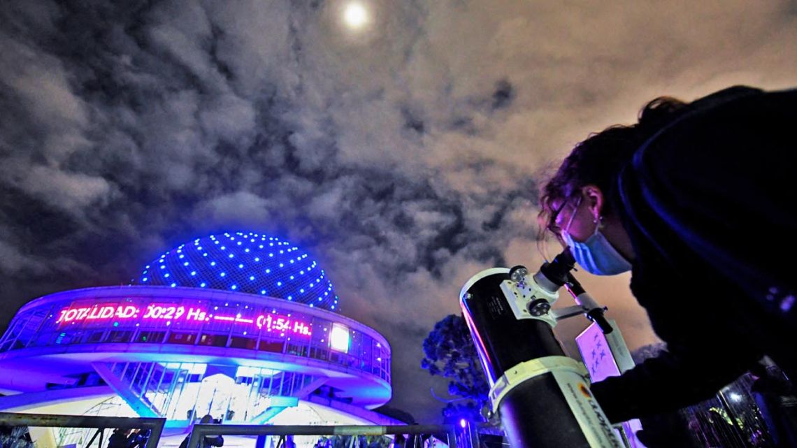 A woman looks at the moon through a telescope during a total lunar eclipse in Buenos Aires, on May 16, 2022.