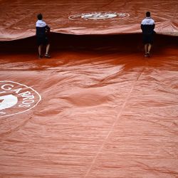 Empleados despliegan una cubierta protectora en la pista Simonne-Mathieu durante un descanso debido a la lluvia en el segundo día del torneo de tenis Roland-Garros Open en París. | Foto:Anne-Christine Poujoulat / AFP