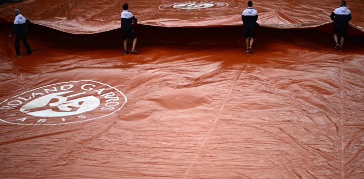 Empleados despliegan una cubierta protectora en la pista Simonne-Mathieu durante un descanso debido a la lluvia en el segundo día del torneo de tenis Roland-Garros Open en París.