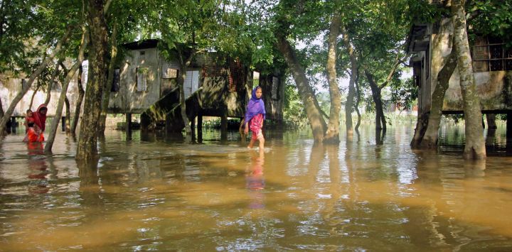 Unas personas vadean una calle inundada tras las fuertes lluvias en Companiganj, Bangladesh.