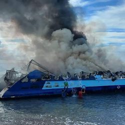 Esta foto tomada y difundida por los guardacostas filipinos muestra a personas arrojando cubos de agua sobre un ferry en llamas que se había incendiado cerca de la ciudad de Real, en la provincia de Quezón. | Foto:Handout / Guardacostas de Filipinas / AFP