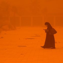 Una mujer consulta un teléfono mientras camina en medio de una fuerte tormenta de polvo en la ciudad de Kuwait. | Foto:YASSER AL-ZAYYAT / AFP