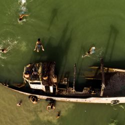 Esta vista aérea muestra a unos niños saltando y nadando junto a un antiguo barco hundido en el canal Shatt al-Arab, formado en la confluencia de los ríos Éufrates y Tigris, en la ciudad de Basora, en el sur de Irak. | Foto:HUSSEIN FALEH / AFP