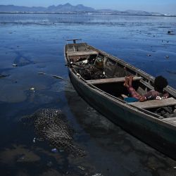 Un hombre se sienta en un bote rodeado de agua contaminada en un río que desemboca en la Bahía de Guanabara, en Río de Janeiro, Brasil. | Foto:CARL DE SOUZA / AFP
