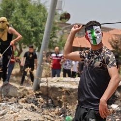 Un manifestante palestino enmascarado lanza piedras junto a otros en medio de enfrentamientos con las fuerzas de seguridad israelíes tras los altercados registrados con colonos israelíes en el pueblo de Urif, al sur de Nablus, en la Cisjordania ocupada. | Foto:JAAFAR ASHTIYEH / AFP