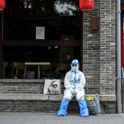 Un trabajador sanitario con equipo de protección descansa frente a un restaurante cerrado en Pekín. | Foto:JADE GAO / AFP