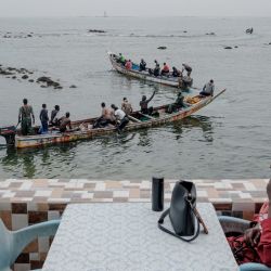 Una mujer se sienta en una marisquería a esperar su comida mientras ve cómo las piraguas se marchan después de vender sus capturas a los restaurantes que se encuentran a lo largo del agua en Dakar, Senegal. | Foto:GUY PETERSON / AFP