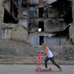 Una niña pasa con un monopatin por delante de un edificio residencial destruido en el pueblo de Horenka, en la región de Kiev, en medio de la invasión rusa de Ucrania. | Foto:SERGEI CHUZAVKOV / AFP