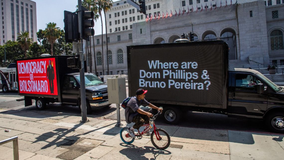 People walk by a truck with messages about British journalist Dom Phillips and Brazilian Indigenous affairs specialist Bruno Pereira, who are missing in the Amazon rainforest, in front of LA City Hall in Los Angeles, California, on June 08, 2022. Leaders from North and South America are gathering in Los Angeles for the ninth Summit of the Americas.