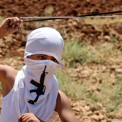 Un joven palestino enmascarado con un pañuelo que muestra un rifle de asalto balancea un tirachinas mientras lanza piedras durante los enfrentamientos con las fuerzas israelíes tras una manifestación contra el establecimiento de puestos de avanzada israelíes, en Beit Dajan, al este de Nablus en la Cisjordania ocupada. | Foto:JAAFAR ASHTIYEH / AFP