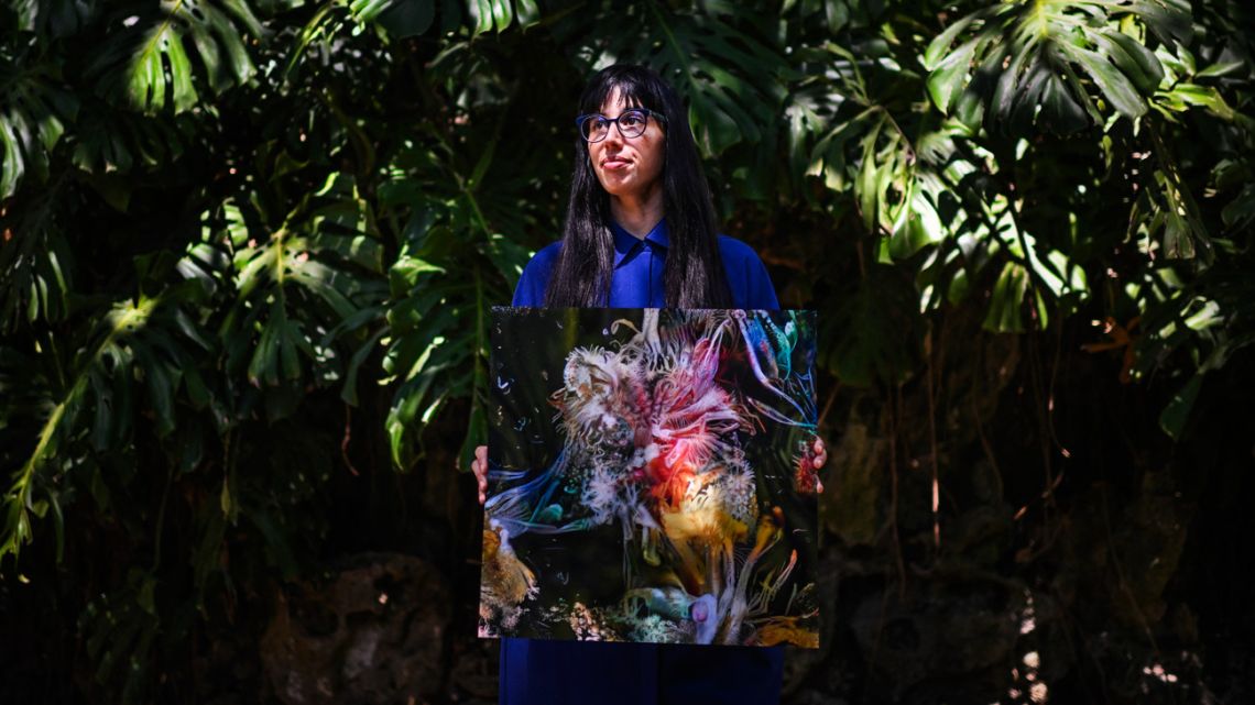 Argentine artist Sofia Crespo holds one of her works as she poses for a photo at the Estrela garden in Lisbon on June 8, 2022. Crespo, who creates her works with the help of artificial intelligence, is part of the 'generative art' movement, where humans create rules for computers which then use algorithms to generate new forms, ideas and patterns. 