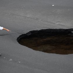 Dos empleados municipales observan un gigantesco agujero en una carretera causado por el colapso de una red de drenaje debido a las fuertes lluvias que afectaron al país, en Villa Nueva, 15 km al sur de Ciudad de Guatemala. | Foto:JOHAN ORDONEZ / AFP