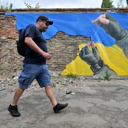 Un hombre pasa con su perro por delante de un mural del artista callejero Sasha Korban que representa las manos de un militar cosiendo partes de la bandera ucraniana, en Kiev. | Foto:SERGEI SUPINSKY / AFP
