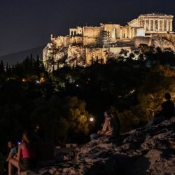 Personas sentadas en una colina frente a la Antigua Acrópolis en Atenas. | Foto:LOUISA GOULIAMAKI / AFP