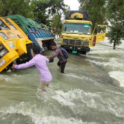 Un grupo de personas vadea los camiones varados en una calle inundada de Sunamganj. - Las inundaciones son una amenaza habitual para millones de personas en las zonas bajas de Bangladesh, pero los expertos afirman que el cambio climático está aumentando su frecuencia, ferocidad e imprevisibilidad. | Foto:Mamun Hossain / AFP