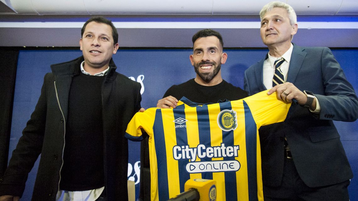 New coach Carlos Tevez holds his new club's shirt up at a Rosario Central press conference, flanked by club officials Raúl Gordillo (left) and the team's vice-president Ricardo Carloni, at the Gigante de Arroyito stadium, in Rosario, Santa Fe Province, on June 21, 2022. 