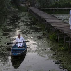 Un hombre rema a bordo de su bote mientras otro camina sobre un puente peatonal en el lago Dal, en la ciudad de Srinagar, capital de verano de Cachemira, administrada parcialmente por India. | Foto:Xinhua/Javed Dar