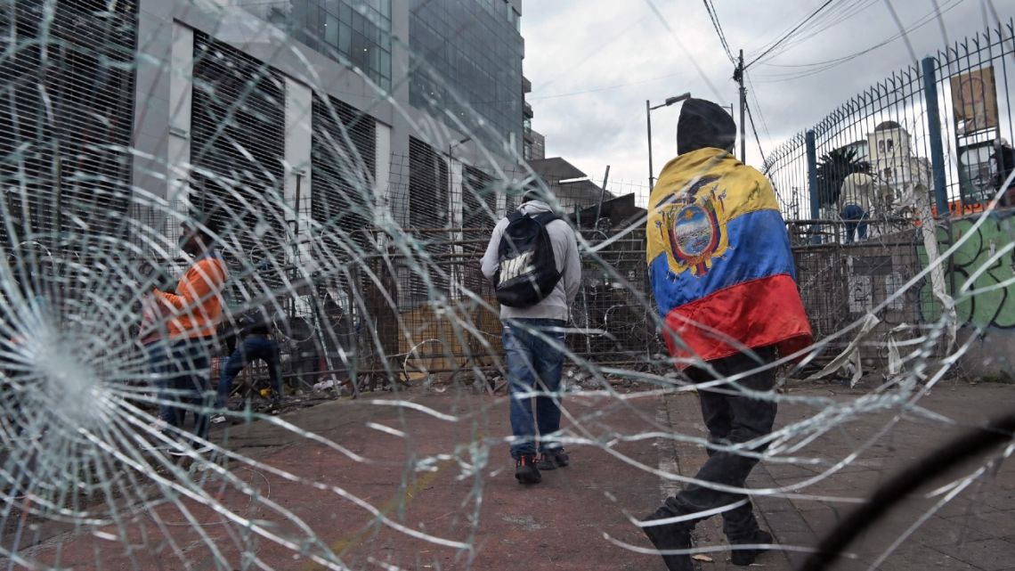 An indigenous man wrapped in an Ecuadorean national flag walks past a broken window put near a barricade in the surroundings of the National Assembly building in Quito on June 26, 2022, in the framework of indigenous-led protests against the government. 