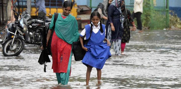 Una mujer junto con una niña de la escuela caminan por un camino inundado luego de una fuerte lluvia en Hyderabad. Noah SEELAM / AFP