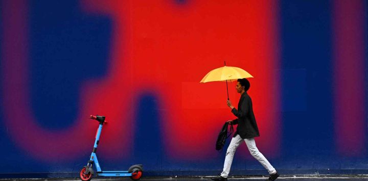 Un peatón se protege de la lluvia con un paraguas mientras pasa frente a un mural publicitario en París. Emmanuel DUNAND / AFP.
