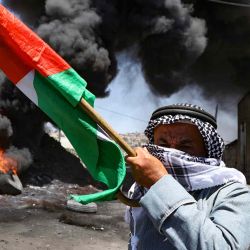 Un anciano palestino sostiene una bandera nacional durante los enfrentamientos con las fuerzas israelíes, en la aldea de Kfar Qaddum. JAAFAR ASHTIYEH / AFP. | Foto:AFP