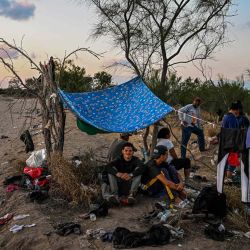 Los migrantes descansan después de cruzar el Río Grande mientras esperan ser detenidos por agentes de la Patrulla Fronteriza mientras los agentes de la Guardia Nacional se sientan en un automóvil al otro lado de la calle (fuera de marco), en Eagle Pass, Texas, en la frontera con México. CHANDAN KHANNA / AFP. | Foto:AFP