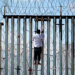 Josué Serrano, un migrante deportado mexicano, cuelga cruces de madera en la cerca fronteriza como parte de una vigilia por los migrantes que murieron mientras migraban a los Estados Unidos, en la frontera entre Estados Unidos y México en Playas de Tijuana. Guillermo Arias / AFP. | Foto:AFP