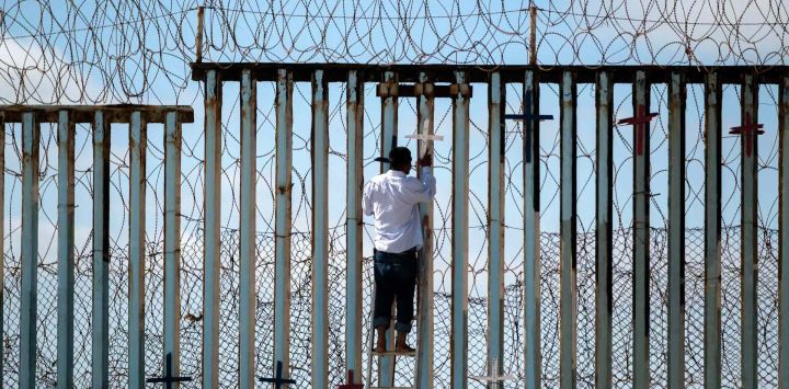 Josué Serrano, un migrante deportado mexicano, cuelga cruces de madera en la cerca fronteriza como parte de una vigilia por los migrantes que murieron mientras migraban a los Estados Unidos, en la frontera entre Estados Unidos y México en Playas de Tijuana. Guillermo Arias / AFP.