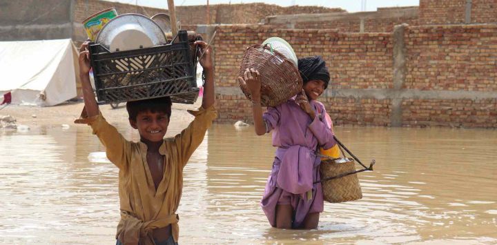 Niños que cargan artículos para el hogar caminan por un área inundada después de una lluvia monzónica en Quetta. Banaras KHAN / AFP.