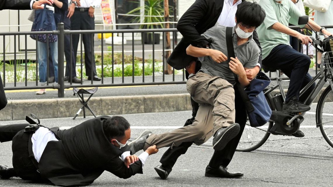 This image received from the Asahi Shimbun newspaper shows a man (centre R) suspected of shooting former Japanese prime minister Shinzo Abe being tackled to the ground by police at Yamato Saidaiji Station in the city of Nara on July 8, 2022. Abe was pronounced dead on July 8, the hospital treating him confirmed, after he was shot at a campaign event in the city of Nara.